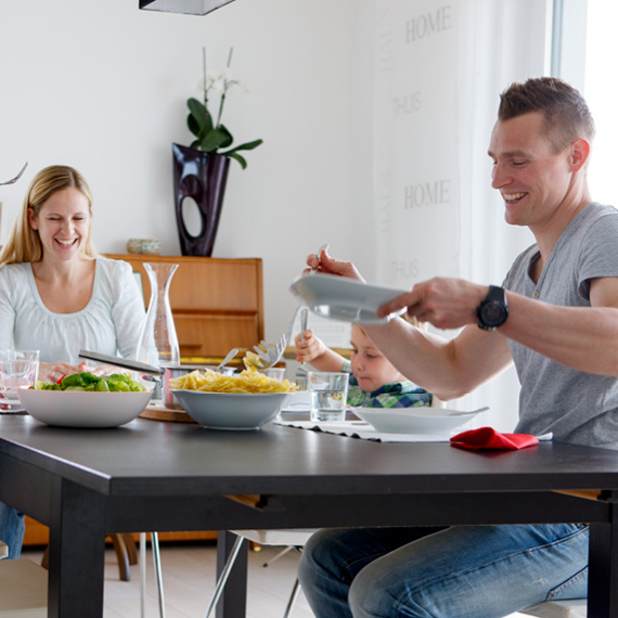 Glückliche, dreiköpfige Familie sitzt zum Essen bei Tisch