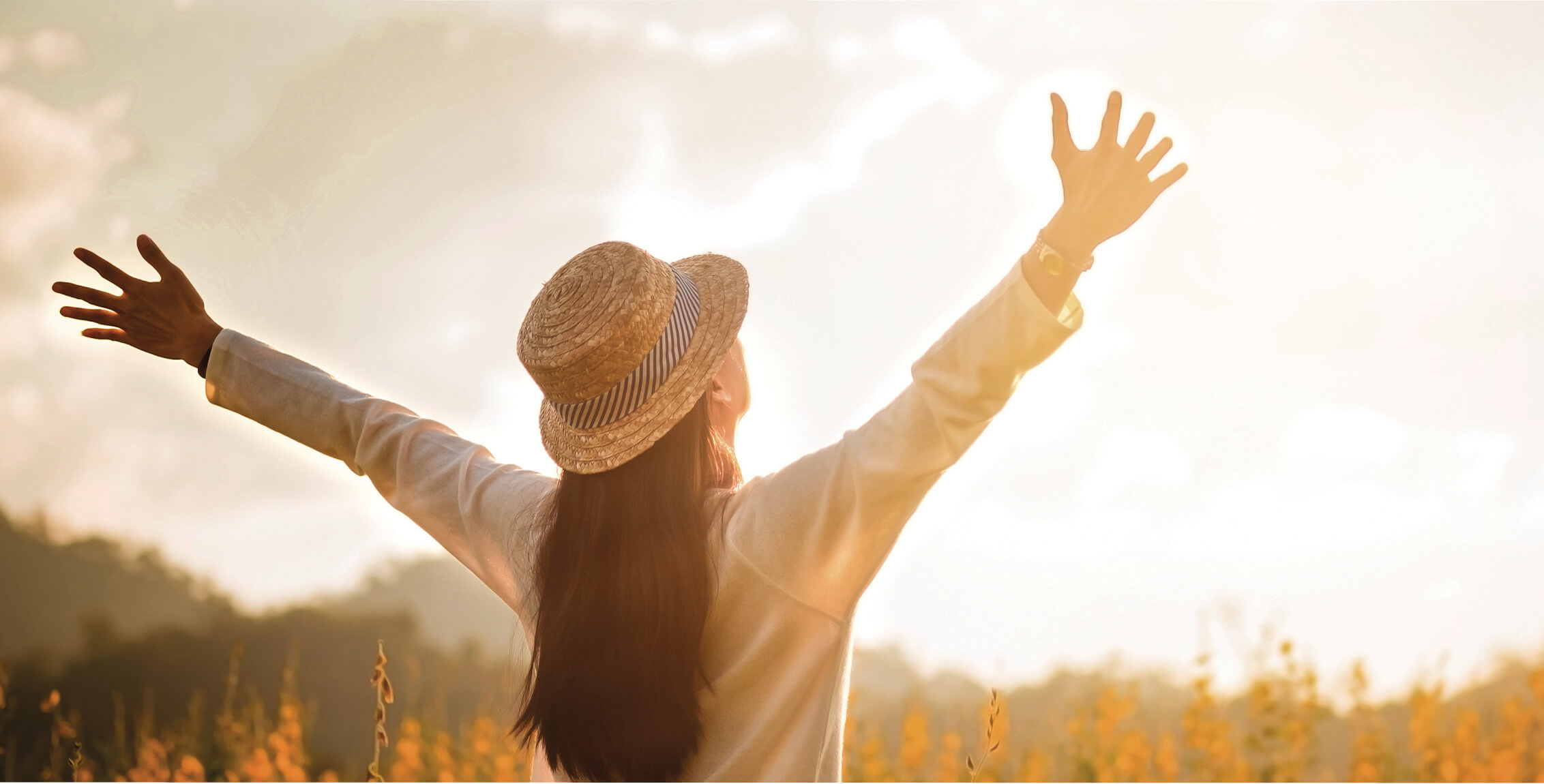 Frau in der Natur streckt ihre Arme der Sonne entgegen.