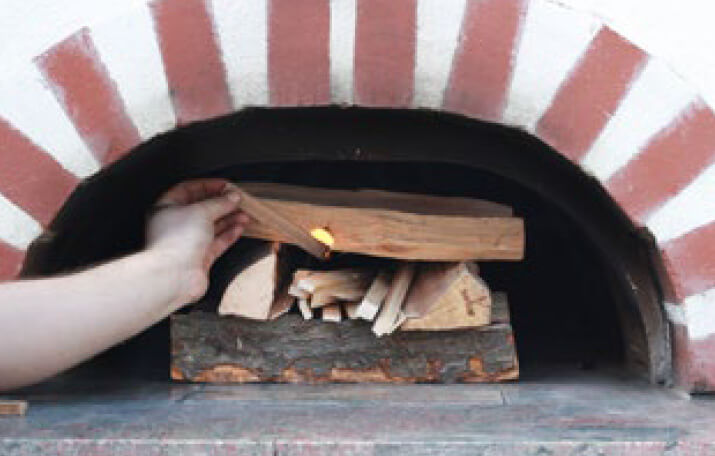 Gestapeltes Holz in einem Holzbackofen wird angezündet.